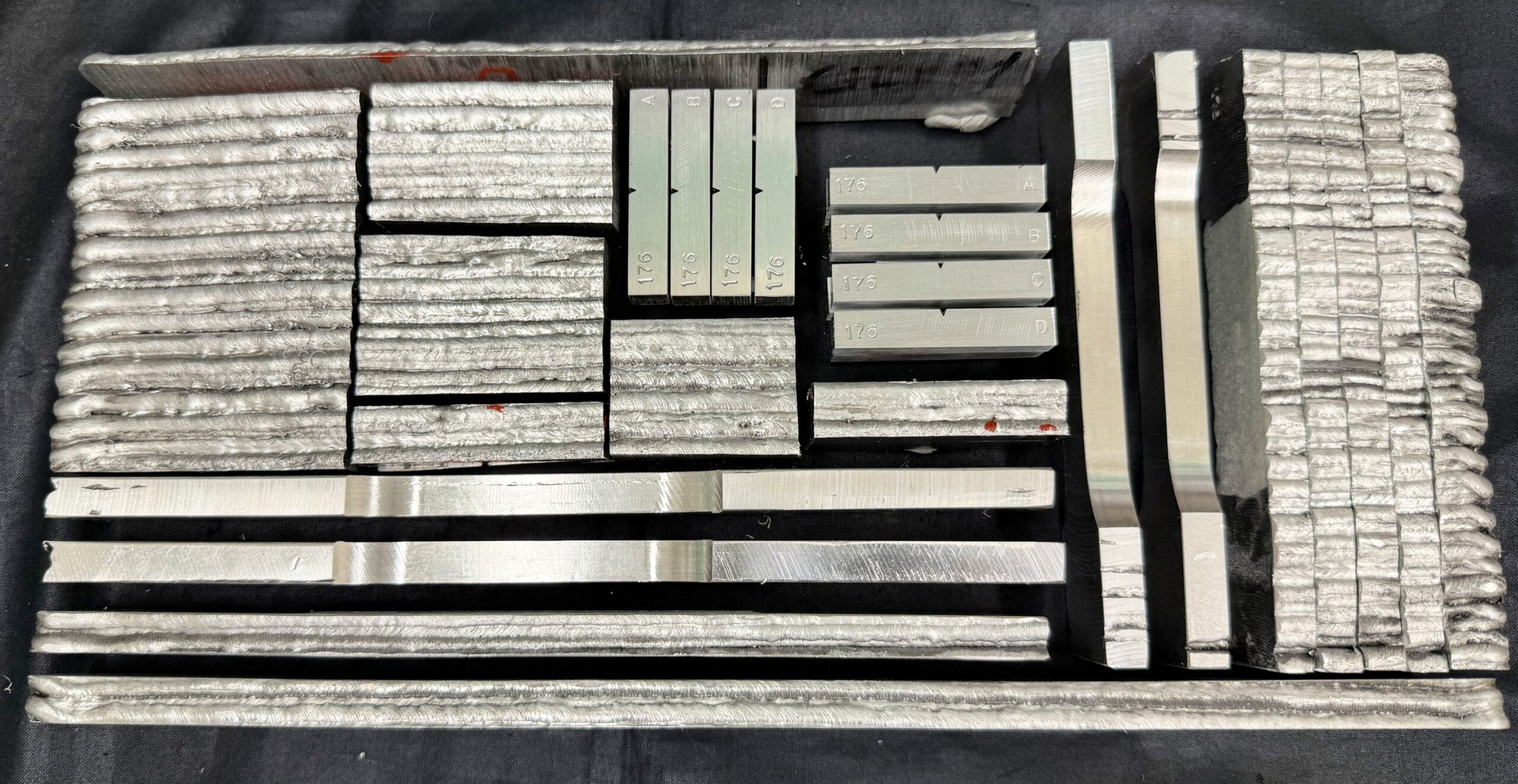 Prepared metal additive manufacturing test specimens showing deposited beads, cut sections and machined samples